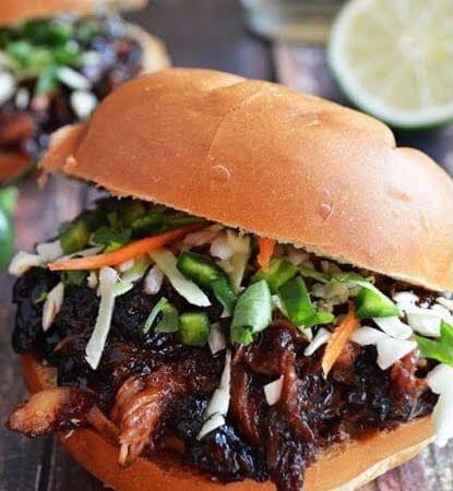A close up of a sandwich with meat and vegetables on a bun on a table.