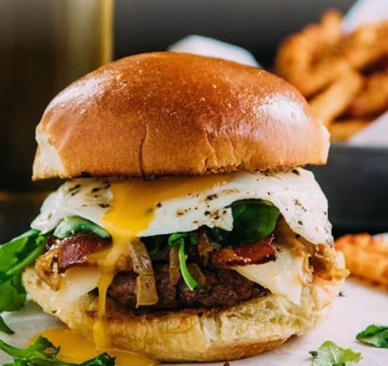 A hamburger with eggs bacon cheese and lettuce on a bun