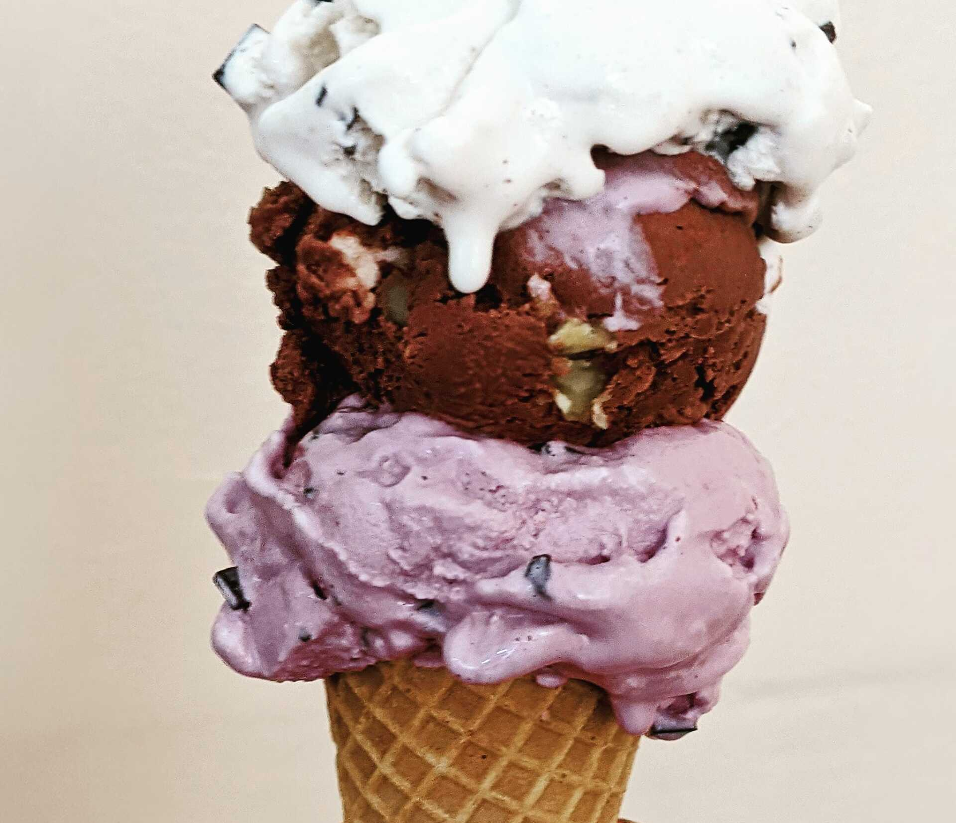 Three scoops of ice cream are stacked on top of each other in a waffle cone.