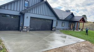 A newly constructed dark blue house with a white garage door, concrete driveway, and unfinished yard under a blue sky.