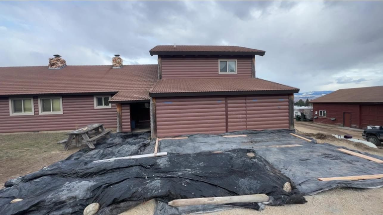 A brown, multi-level building under a cloudy sky with construction plastic laid over a dirt area in the foreground.