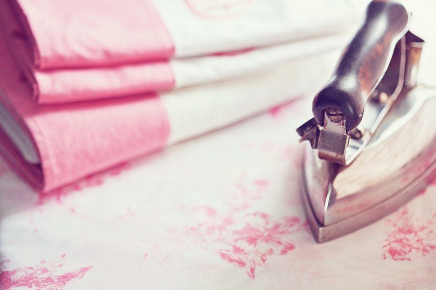 Folded white and pink sheets next to an old iron