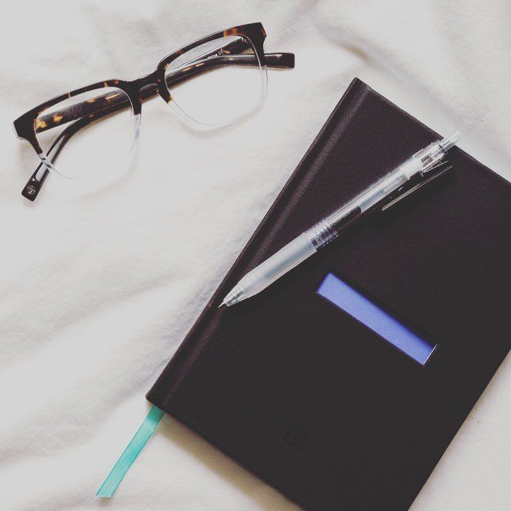 A pair of glasses next to a notebook and pen