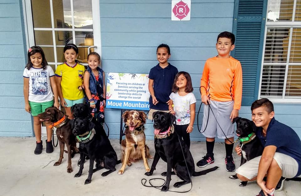 A group of children and their dogs are posing for a picture in front of a house.