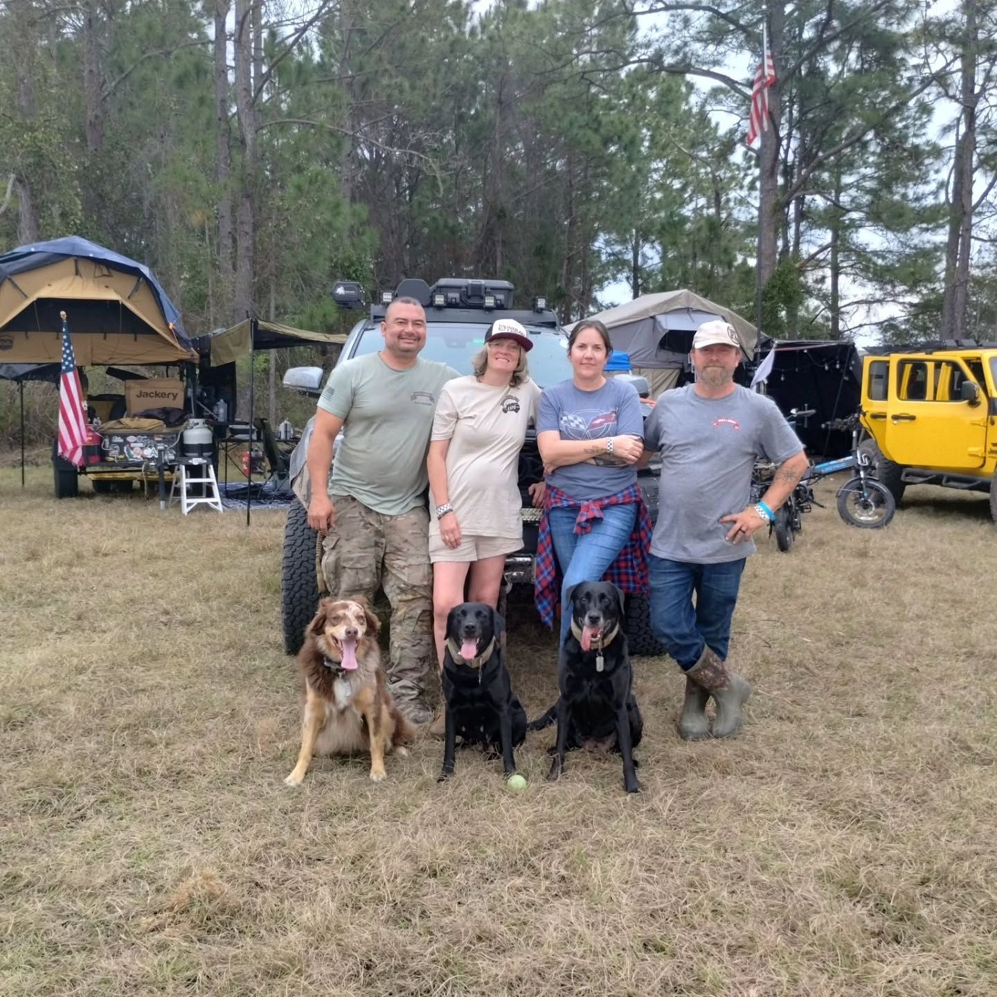 A group of people posing for a picture with their dogs in a field.