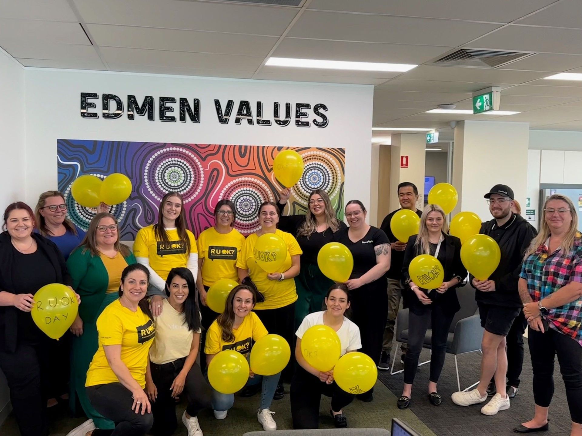 A group of people are posing for a picture in front of a wall that says edmen values.