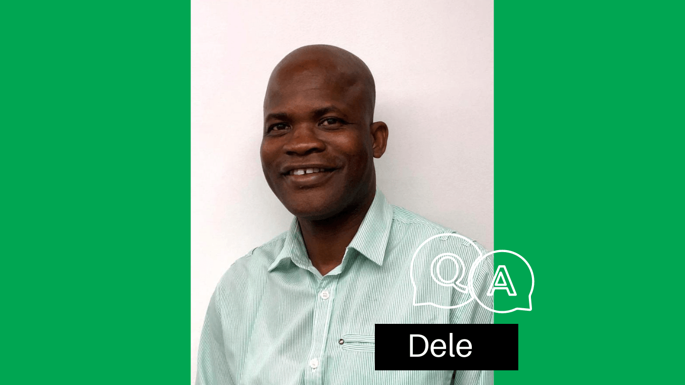 A man in a striped shirt is smiling in front of a green flag.