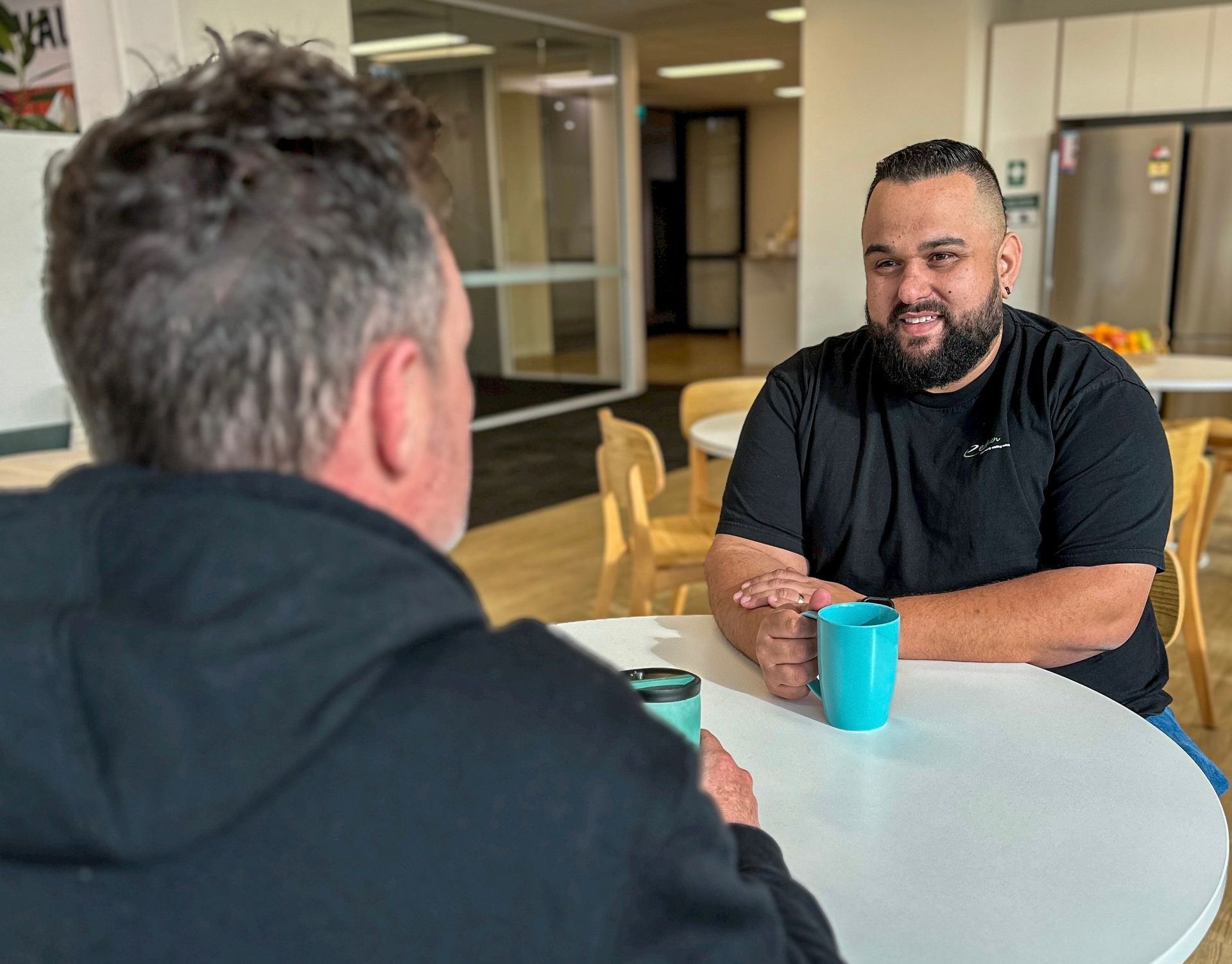 Two men are sitting at a table talking to each other.