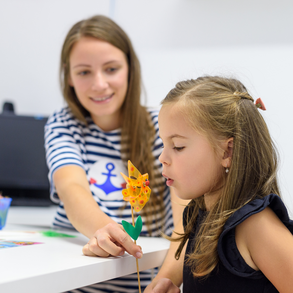 A woman with an anchor on her shirt is playing with a little girl