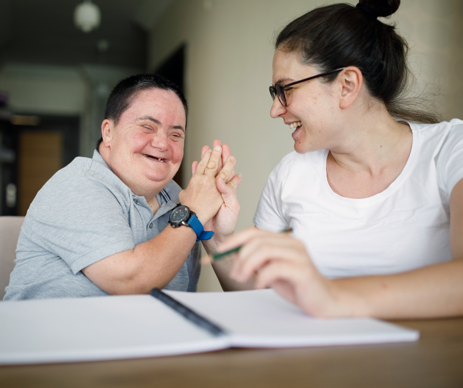 Two women are sitting at a table giving each other a high five.