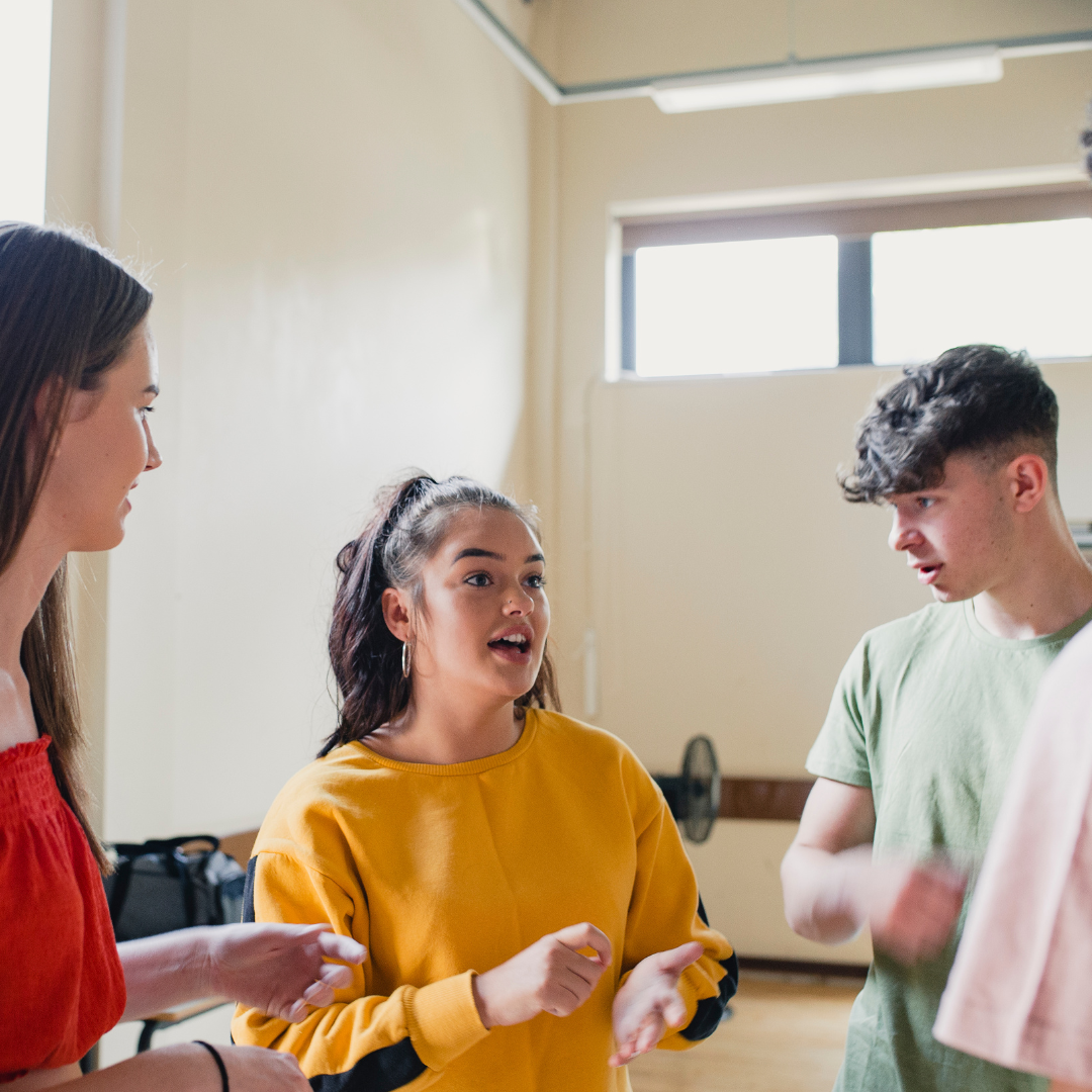 A group of young people are standing in a room talking to each other.