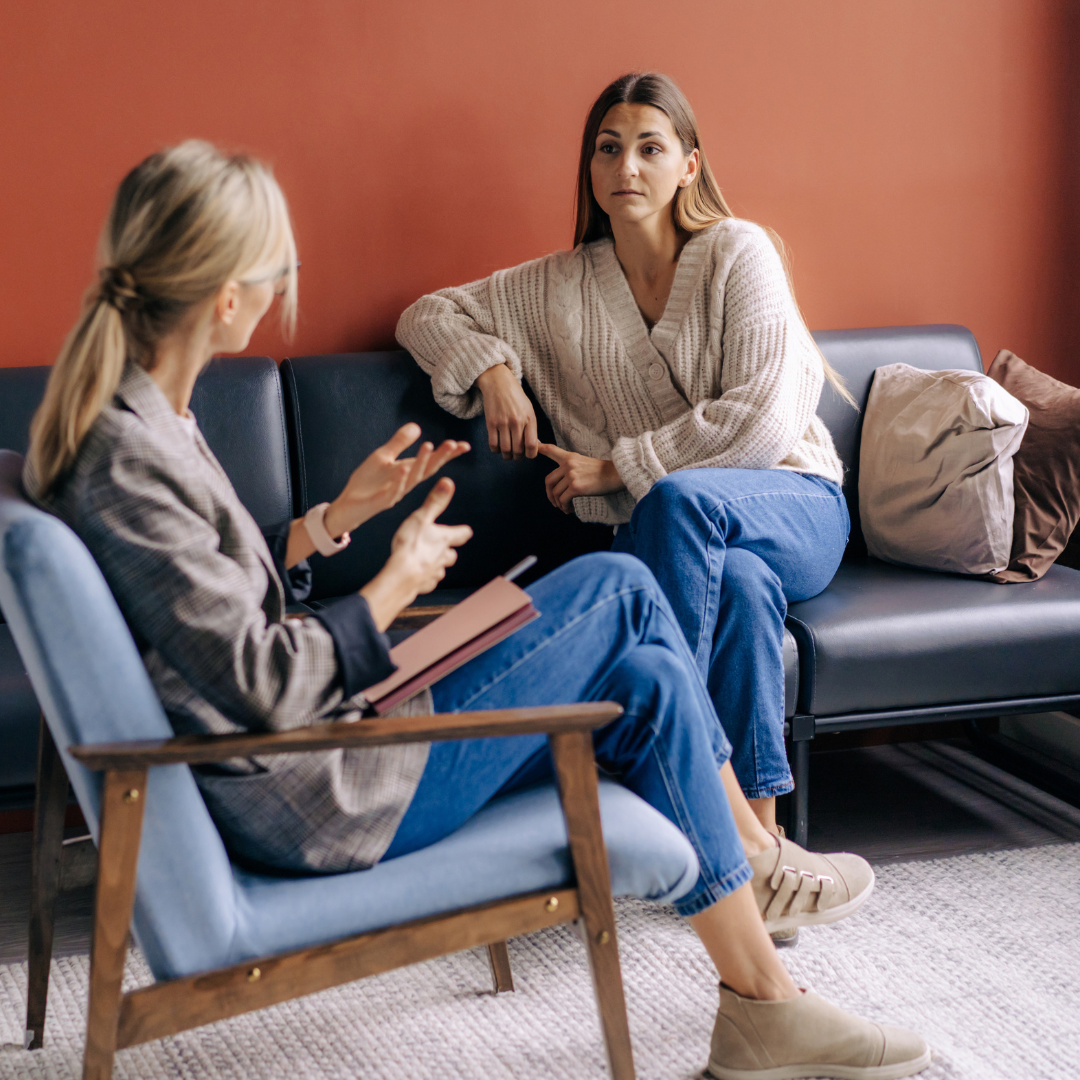 Two women are sitting on a couch talking to each other.