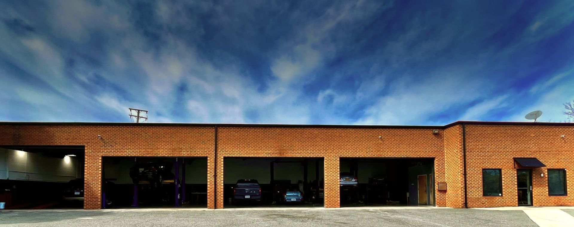 A one-story brick commercial building with four open garage bays under a blue sky with wispy clouds. | Autowerx