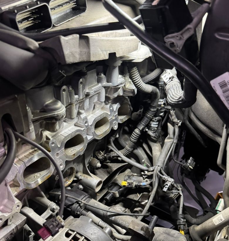 A close-up view inside a car engine bay, showing the intake manifold ports on the engine block and surrounding wiring. | Autowerx