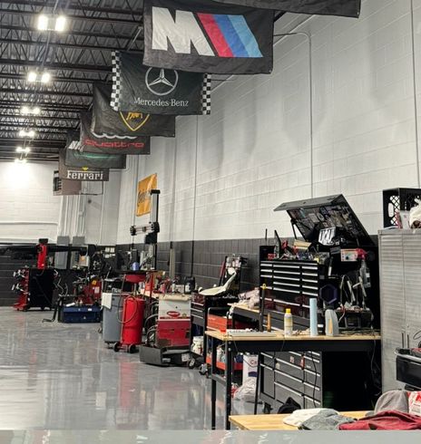 Automotive repair shop featuring hanging banners of luxury car brands and rows of workbenches with various tools. | Autowerx
