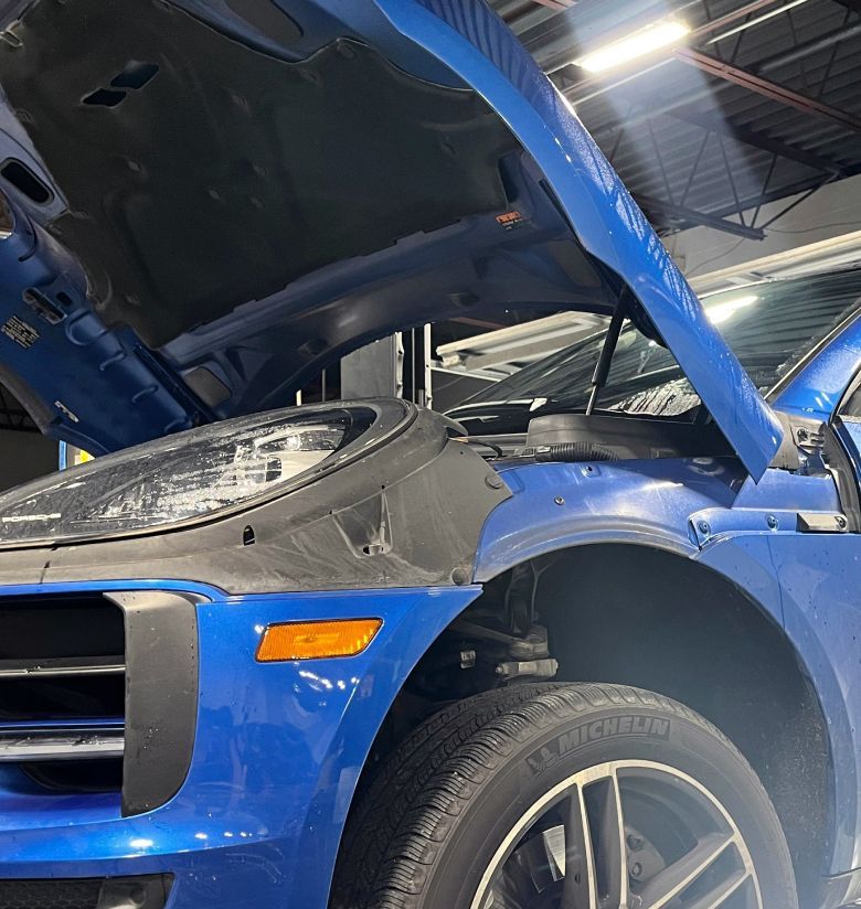 A blue car with its hood open, showing the front wheel, headlight, and interior components in a garage setting. | Autowerx