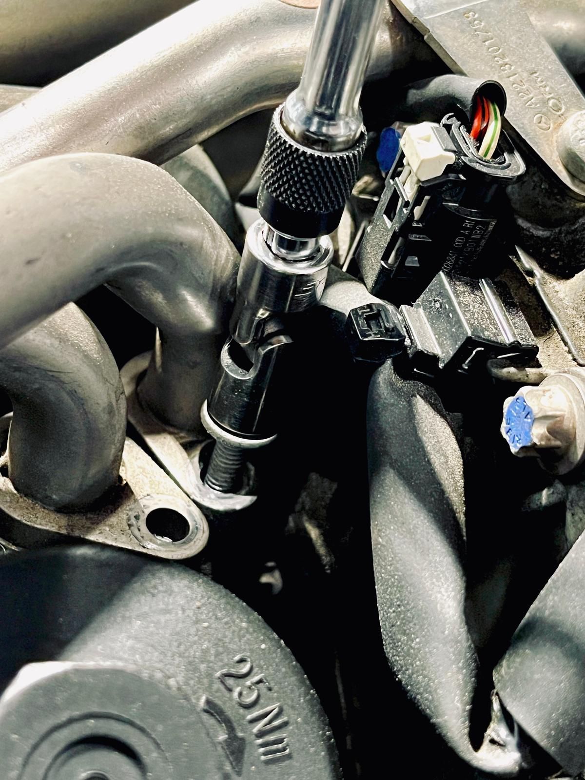 A close-up of a mechanic using a socket wrench with a universal joint to loosen a bolt on an engine component. | Autowerx