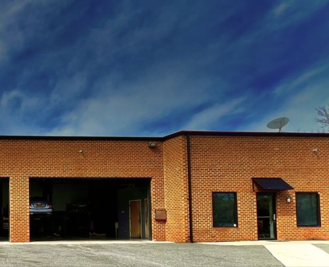 A one-story brick commercial building with four open garage bays under a blue sky with wispy clouds. | Autowerx