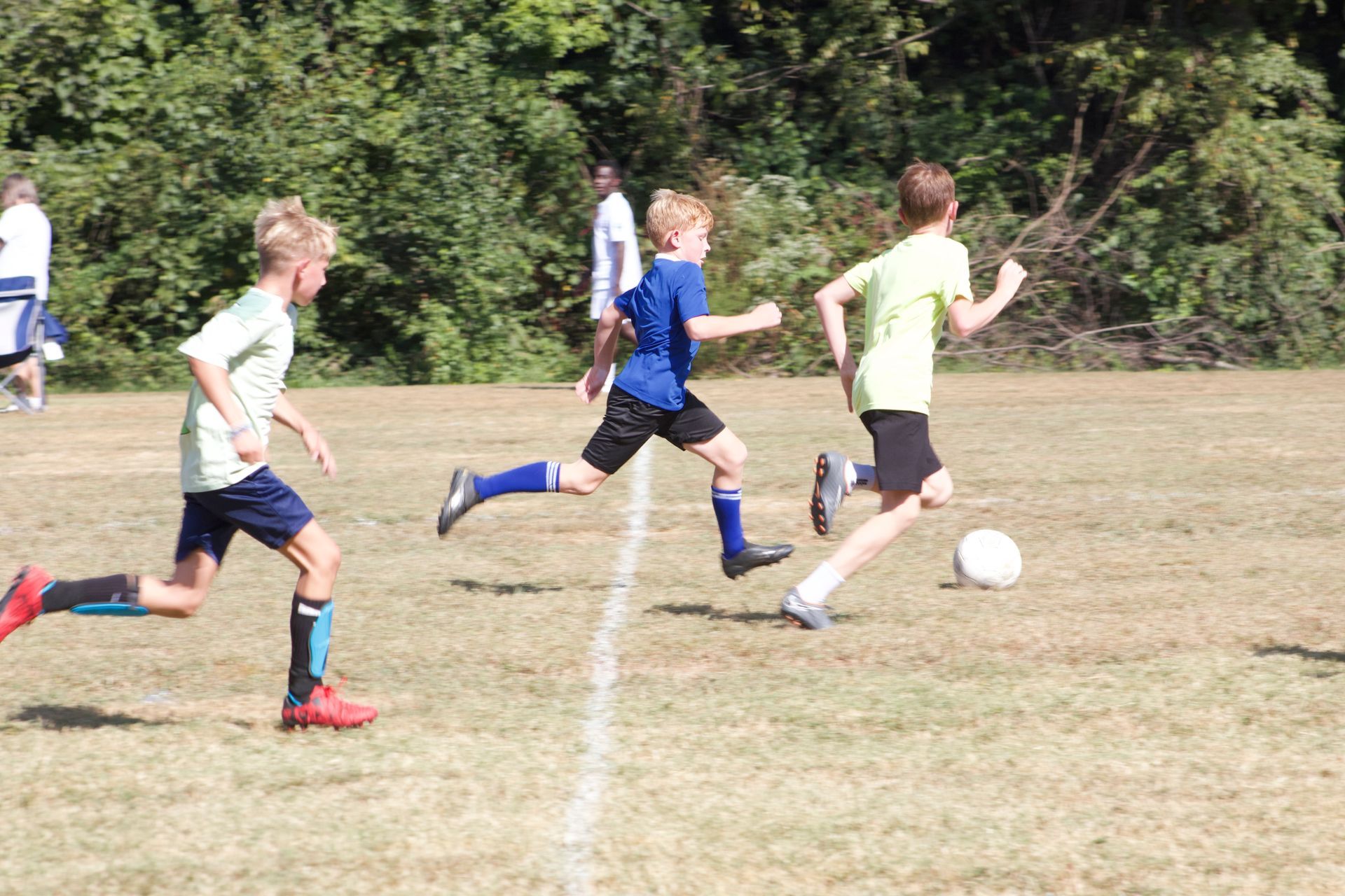 Kids playing soccer on a grassy field, with one player dribbling the ball past two others.