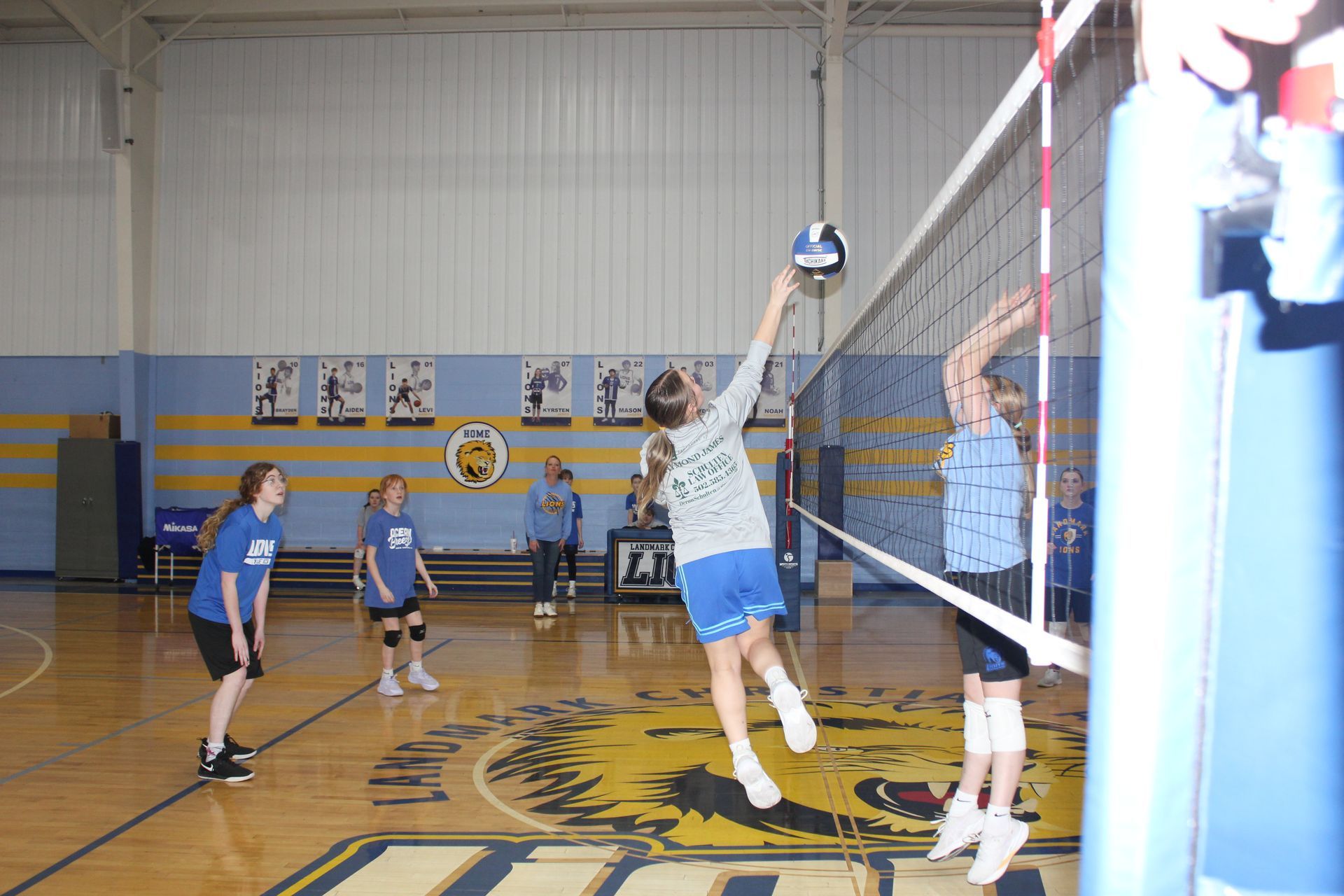 Indoor volleyball game with players jumping at the net in a blue gymnasium