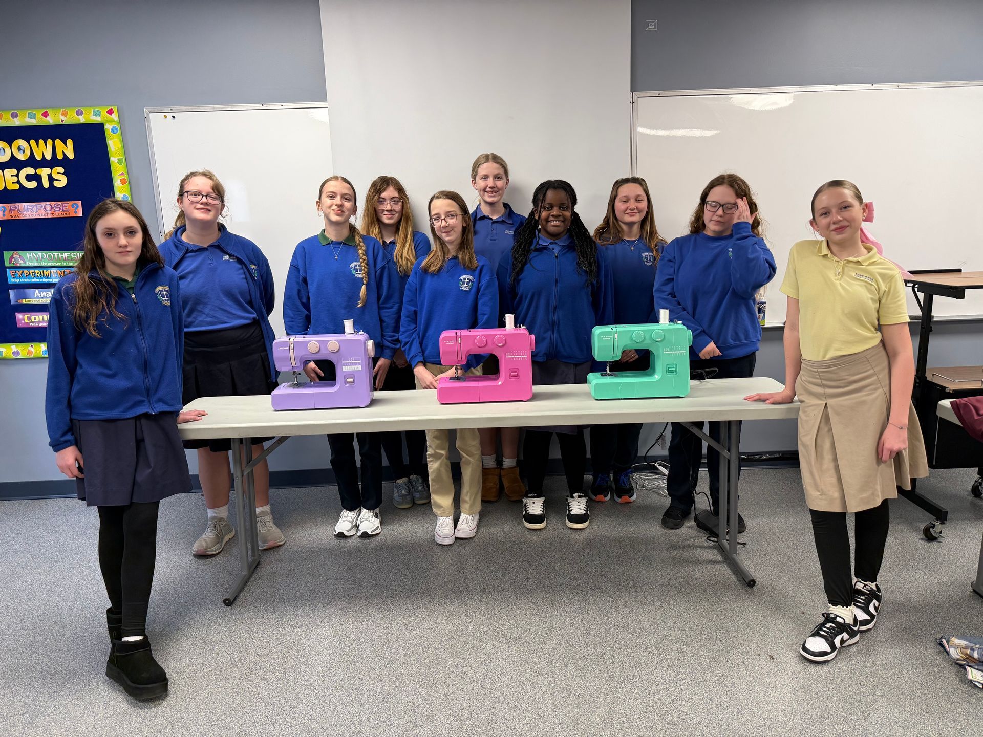 Group of students in blue sweatshirts standing behind three colorful machines in a classroom/lab.