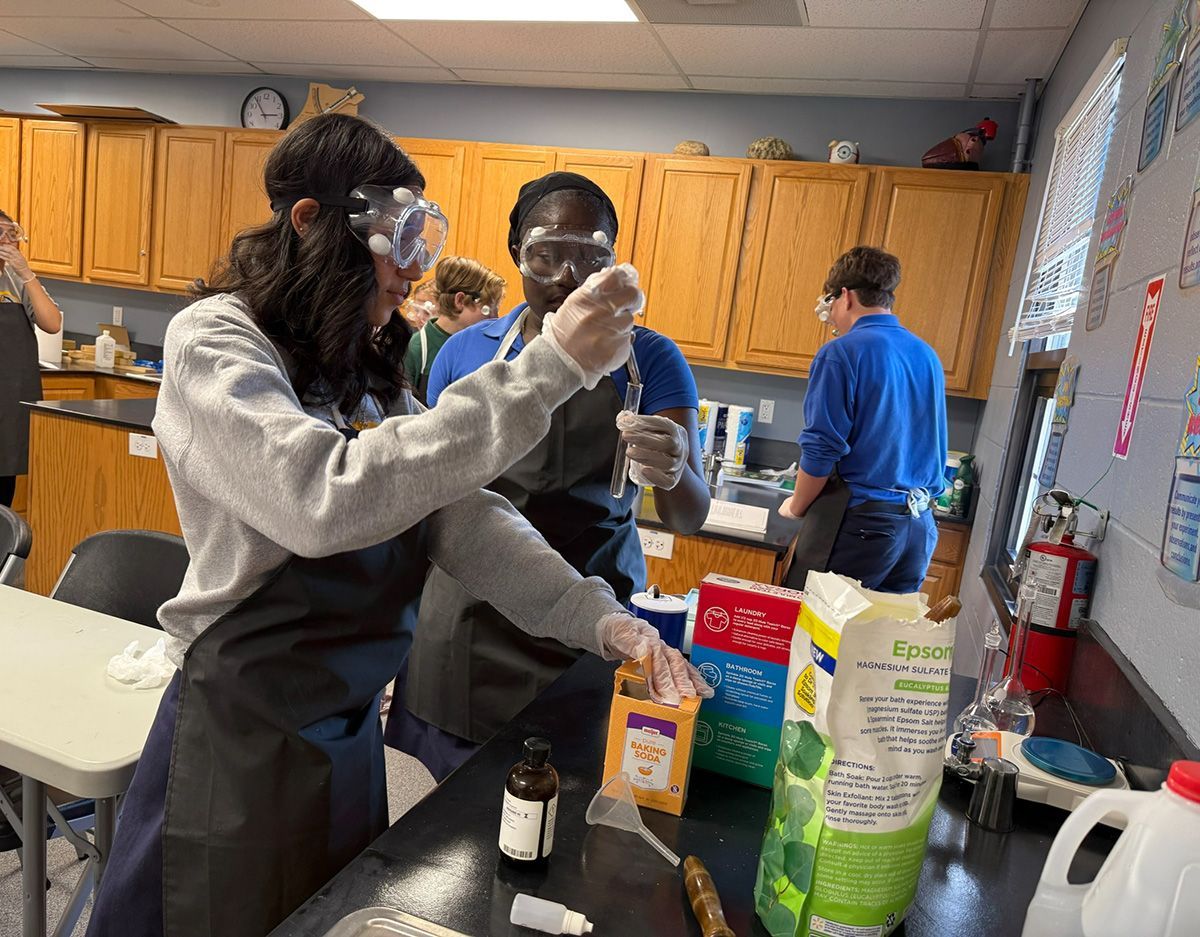 People in a kitchen lab mix ingredients at a counter with bottles, boxes, and bowls.
