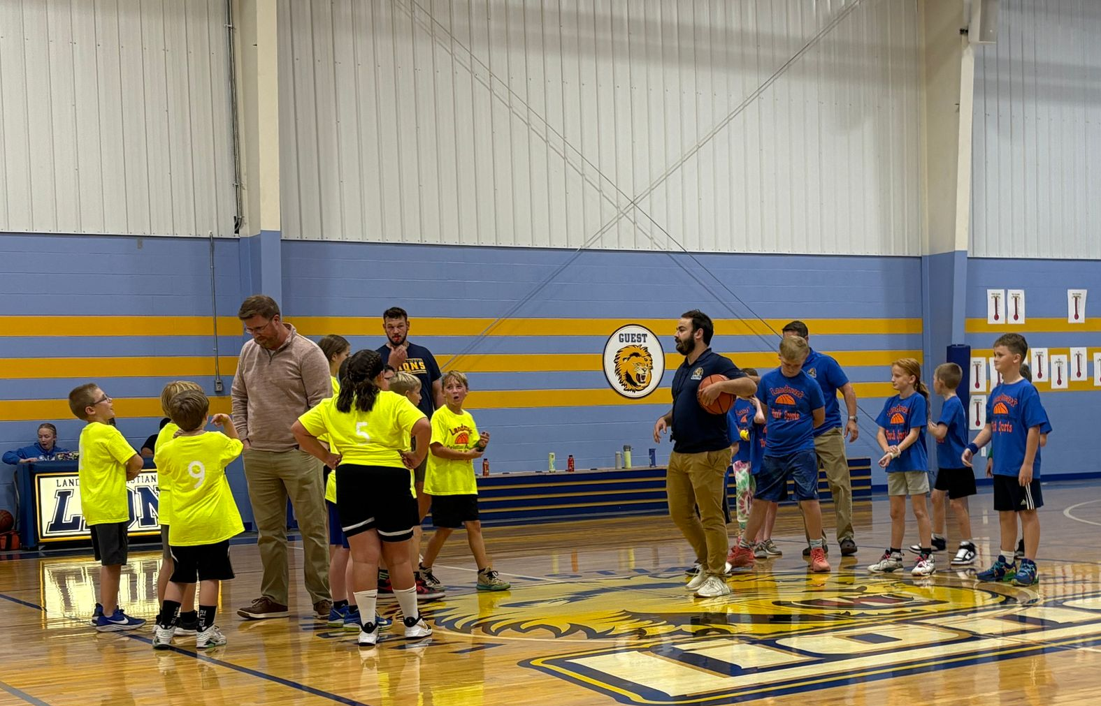 Children in neon yellow and blue shirts line up on a gym floor for a team activity.