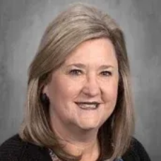 Portrait of a smiling woman with shoulder-length blonde hair against a gray background