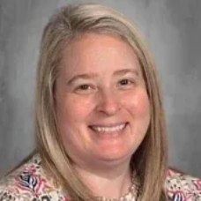 Smiling person with shoulder-length blond hair against a gray background