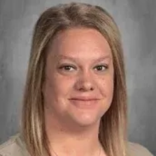 Portrait photo of a person with shoulder-length blonde hair smiling against a gray background