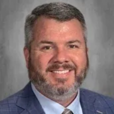 Smiling man in a blue suit jacket and tie against a gray studio backdrop