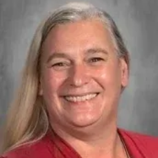 Smiling person with long gray hair in a red top against a gray background