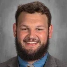 Smiling bearded man in a suit and blue shirt against a gray background