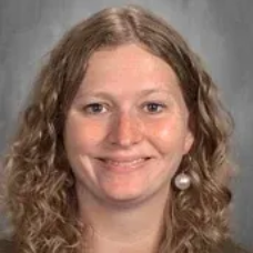 Smiling person with curly hair in front of a gray backdrop
