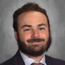 Portrait of a smiling bearded man in a suit and tie against a gray backdrop