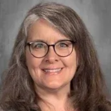 Smiling woman with glasses and gray hair against a neutral gray background