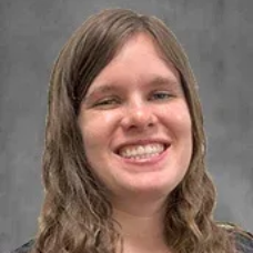 Smiling person with long wavy hair against a gray background