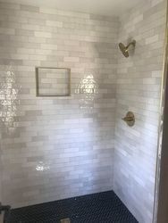 a shower with white tile walls and a black tile floor