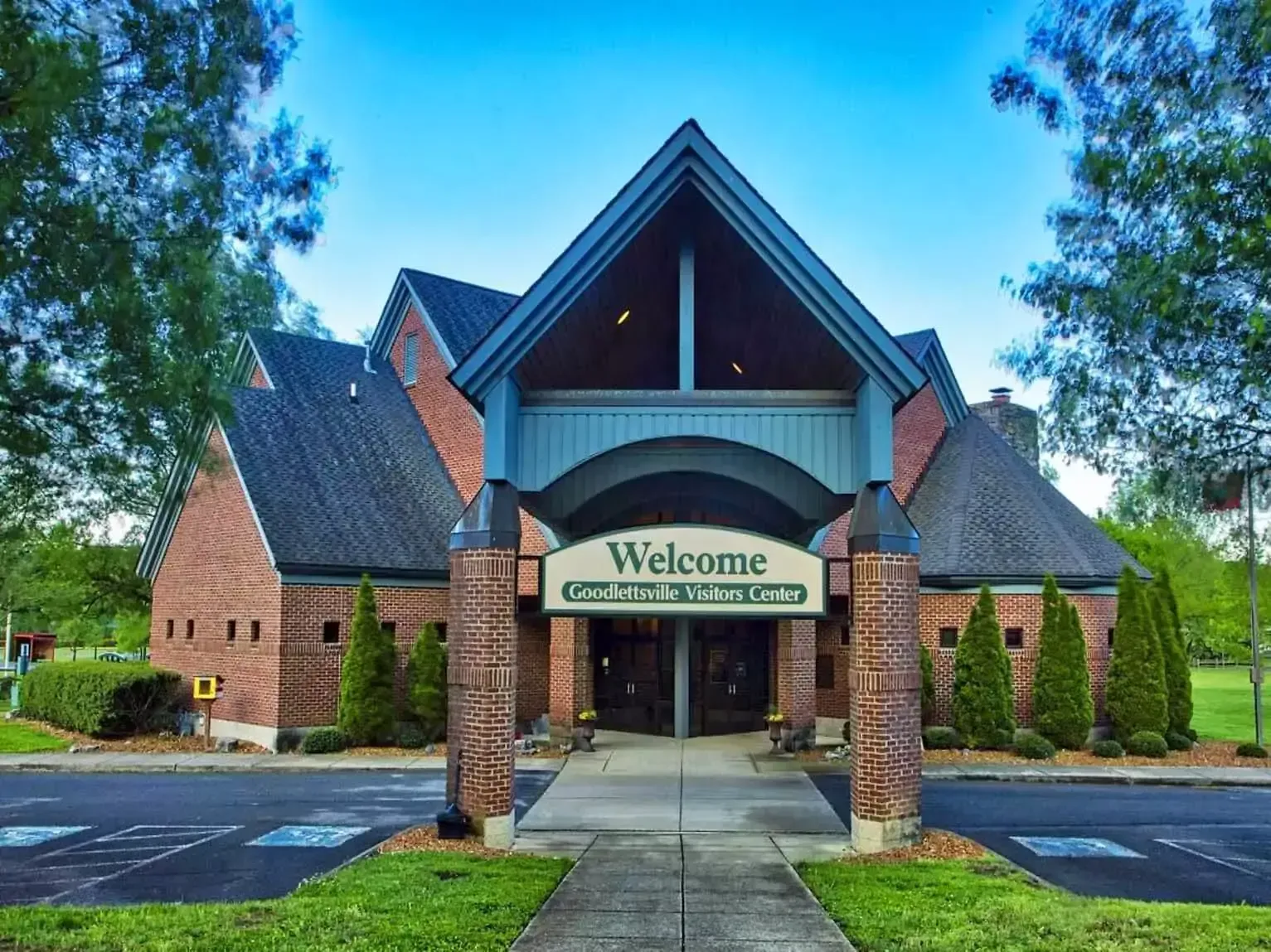 Brick building with a welcome sign above double doors; trees and blue sky background.