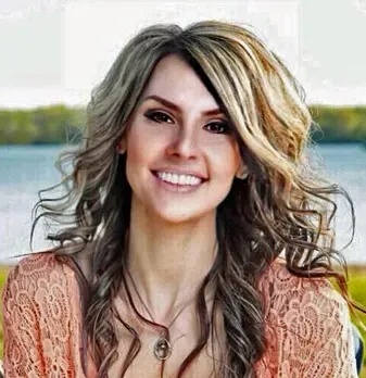 A woman with long hair and a necklace is smiling for the camera.