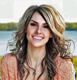 A woman with long hair and a necklace is smiling for the camera.