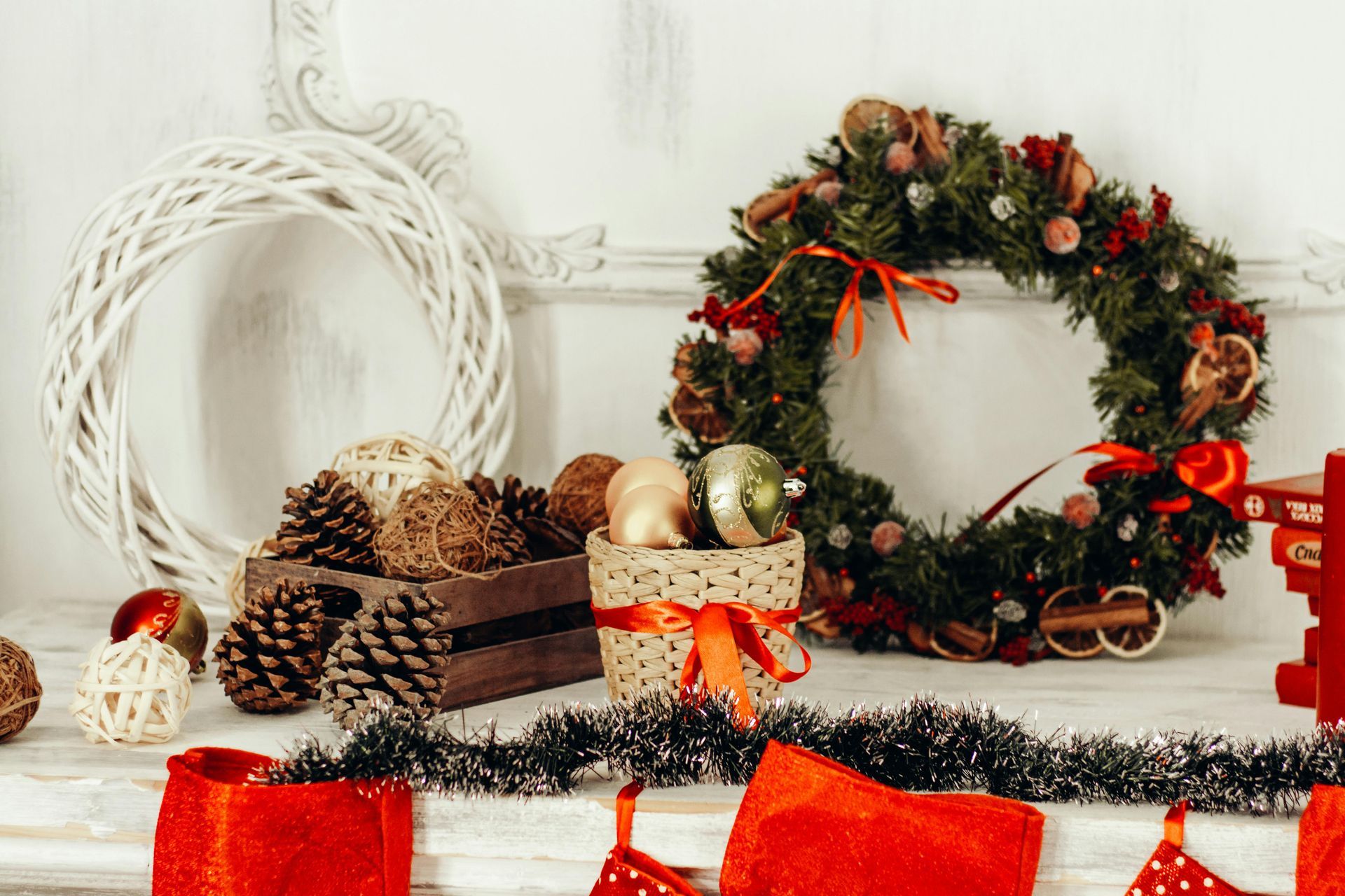 Christmas decorations on a white mantel: wreath, ornaments, pinecones, wooden box, ribbon, and garland.