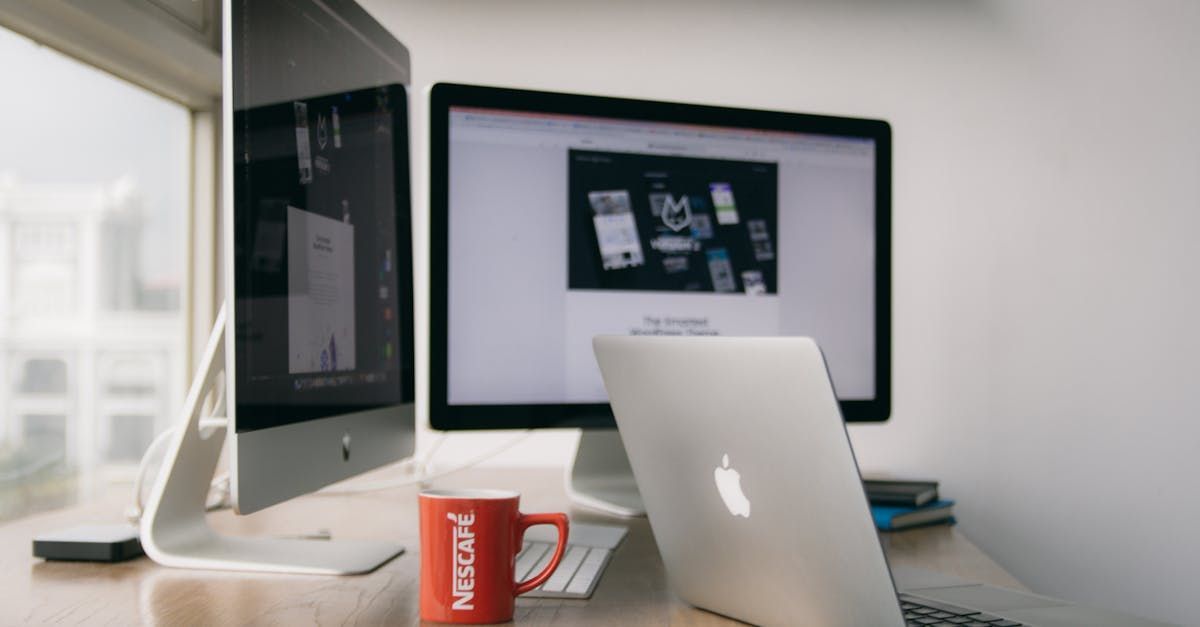 A laptop computer is sitting on a desk next to two monitors.