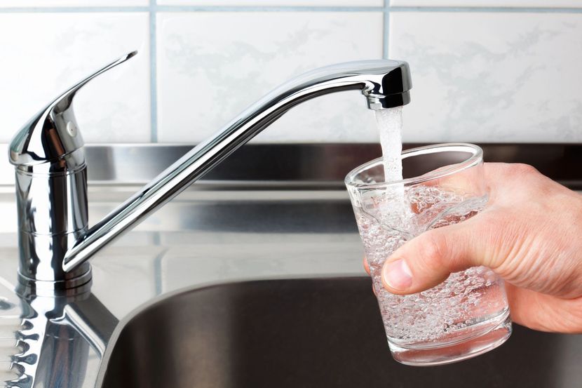 Versare manualmente l'acqua dal rubinetto della cucina in un bicchiere trasparente sopra un lavandino.