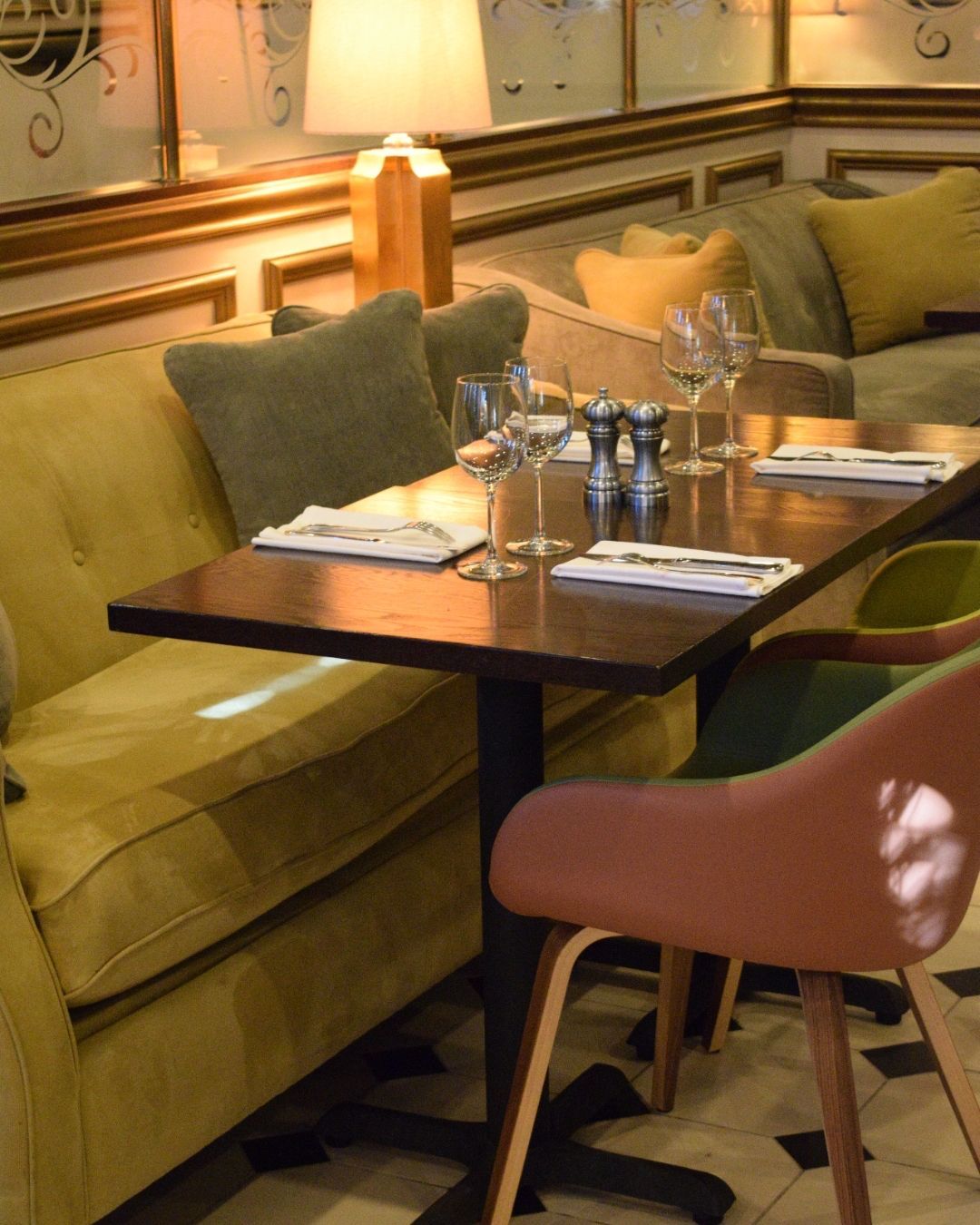 Table set for dining with a yellow sofa, pink chair, and glasses in a restaurant.