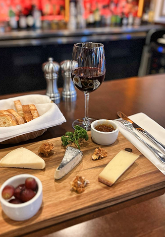 Cheese board with red wine, crackers, and grapes on a wooden table in a restaurant.