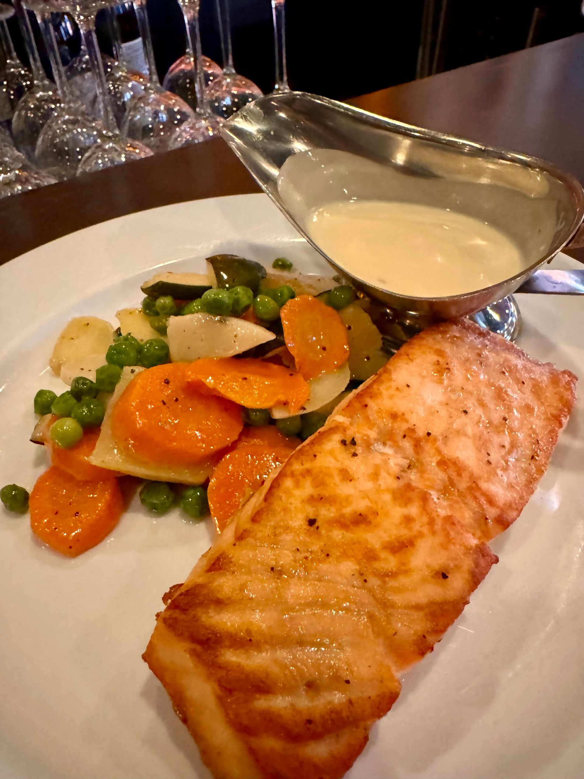 Salmon fillet with vegetables and sauce in a silver gravy boat on a white plate.