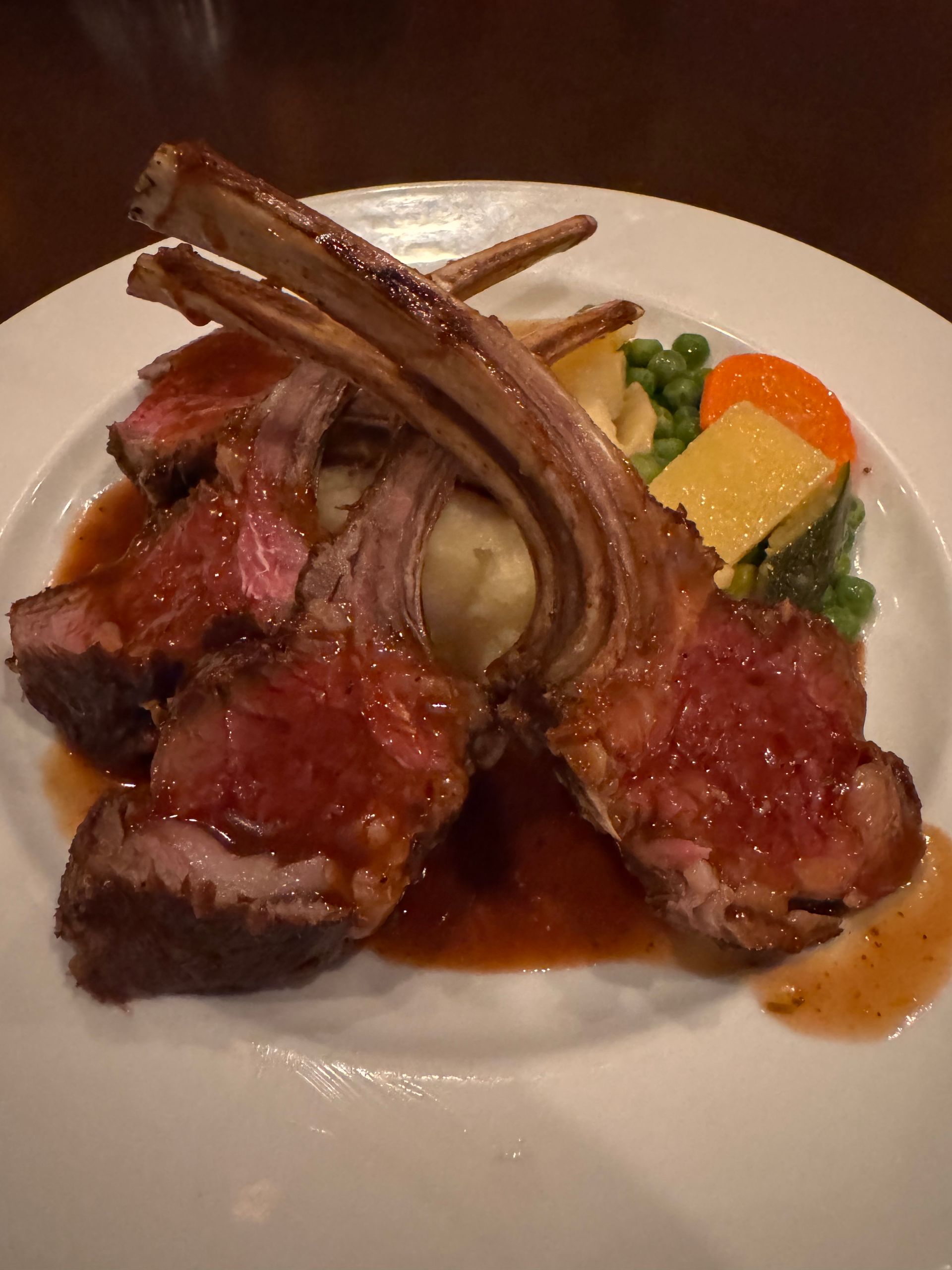 Rack of lamb with mashed potatoes, peas, carrots, and gravy on a white plate.