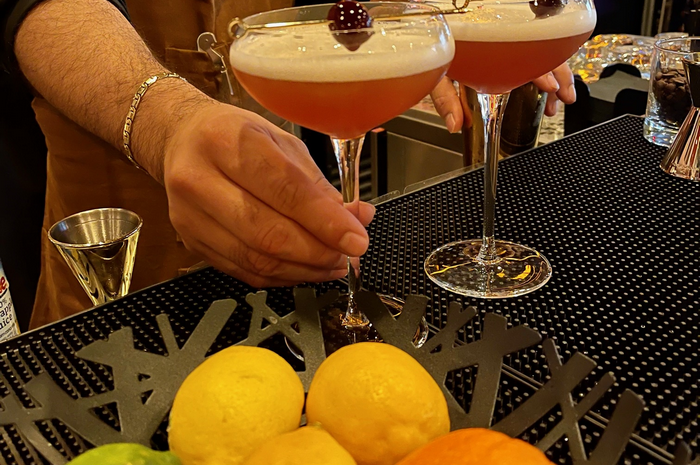 Bartender holding a cocktail with cherry garnish; lemons and oranges in foreground.