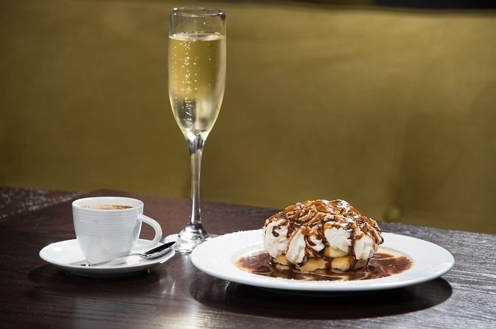 Dessert plate with chocolate sauce and cream, espresso, and champagne glass on a dark table.